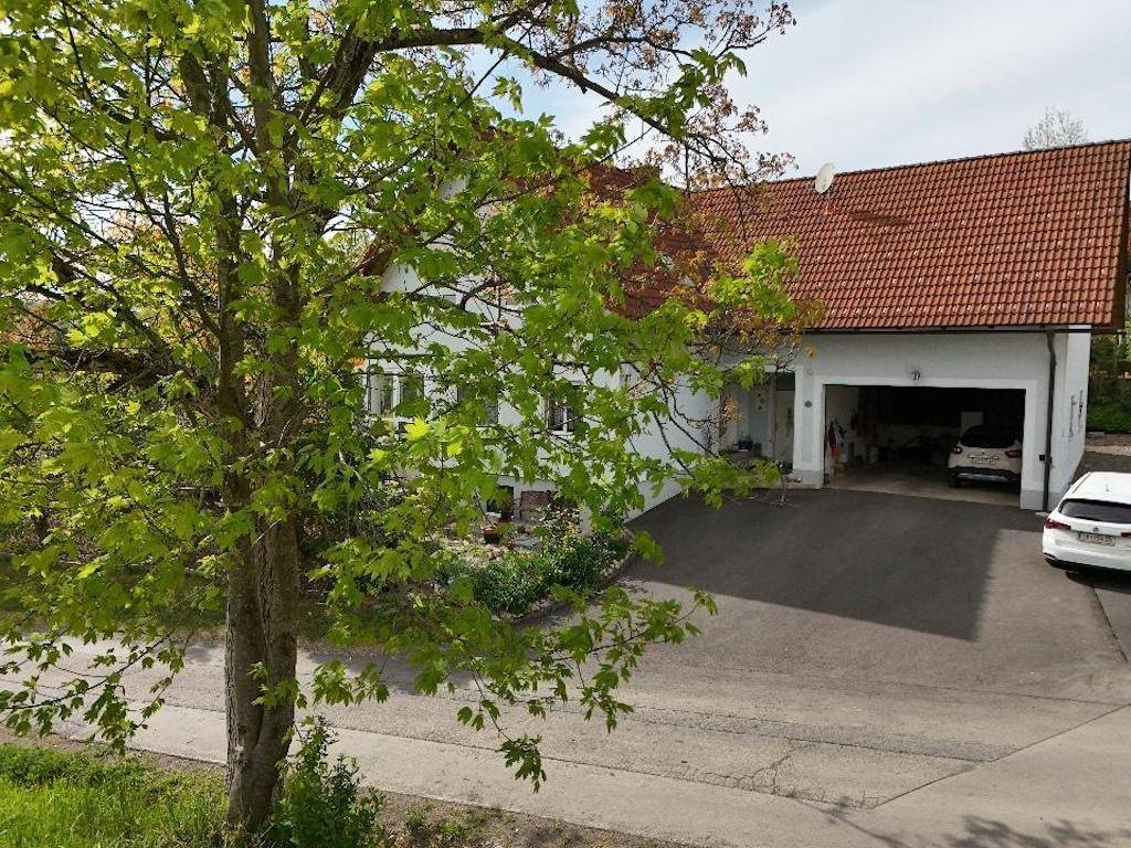 Weißes Haus mit rotem Ziegeldach, integrierter Garage und gepflegter Auffahrt, umgeben von Grün.