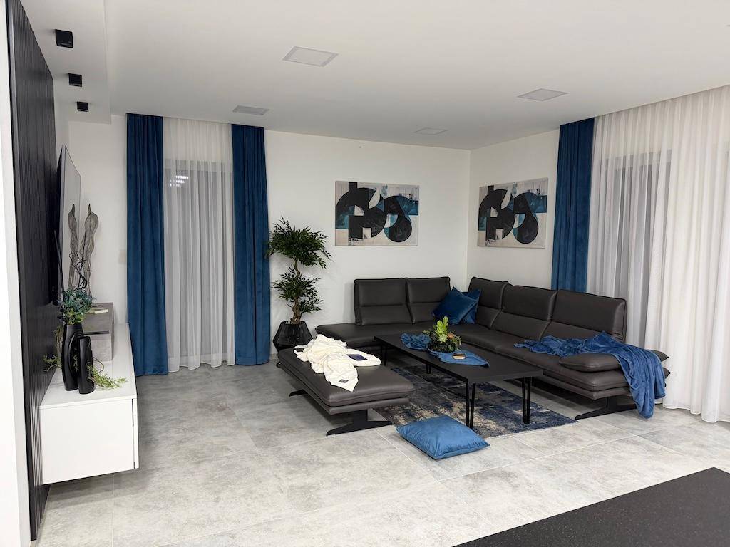 Geräumiges Wohnzimmer mit bequemer Eckcouch, Couchtisch und zwei modernen Kunstwerken an der Wand.
