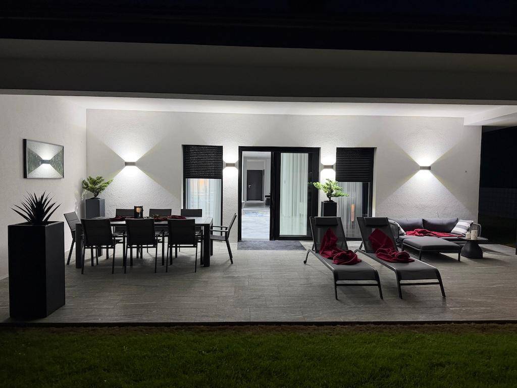 Beleuchtete überdachte Terrasse am Abend mit Esstisch, Lounge-Möbeln und stilvoller Außenbeleuchtung.