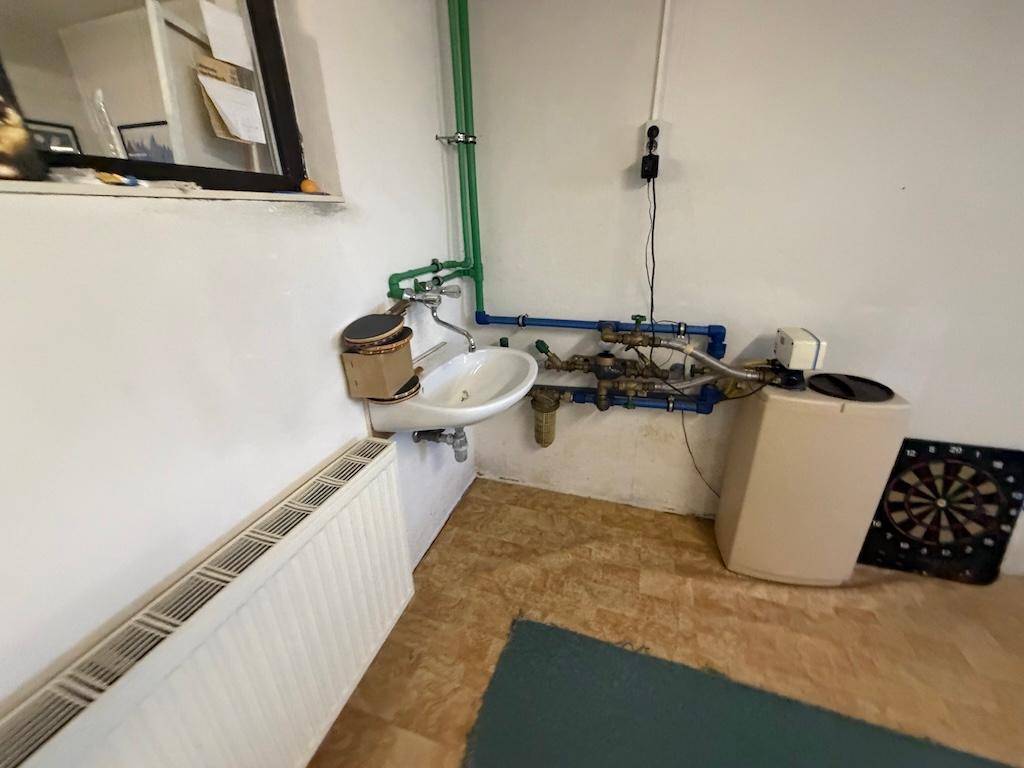Praktischer Hauswirtschaftsraum mit Waschbecken, Heizkörper und sichtbaren Installationen.