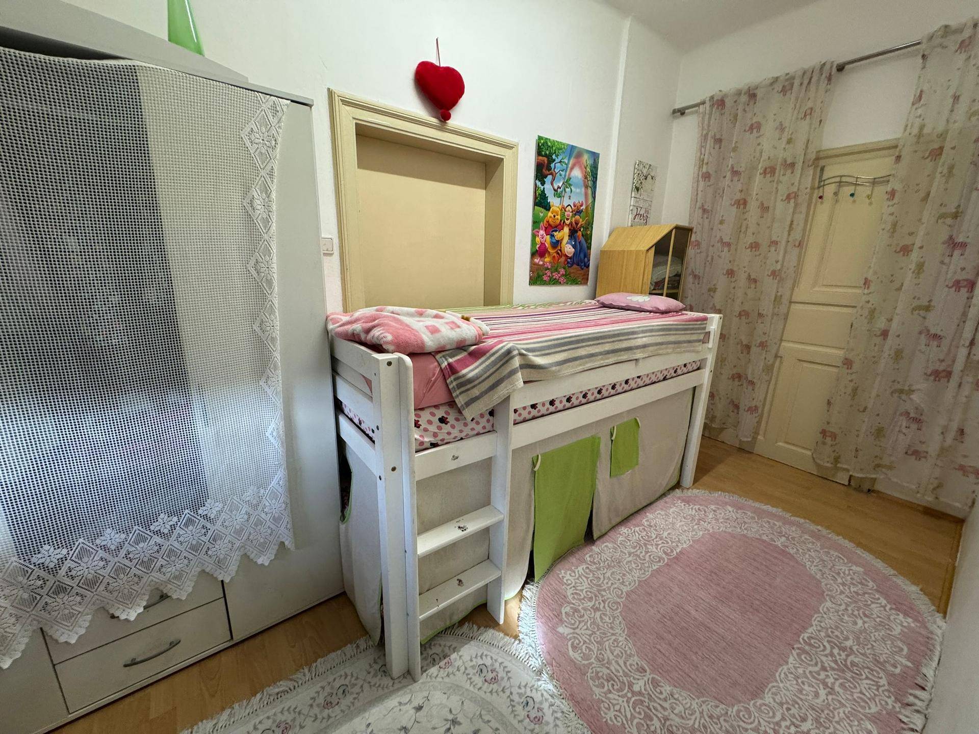 Kinderzimmer mit Hochbett, farbenfrohem Teppich und einem Kleiderschrank.