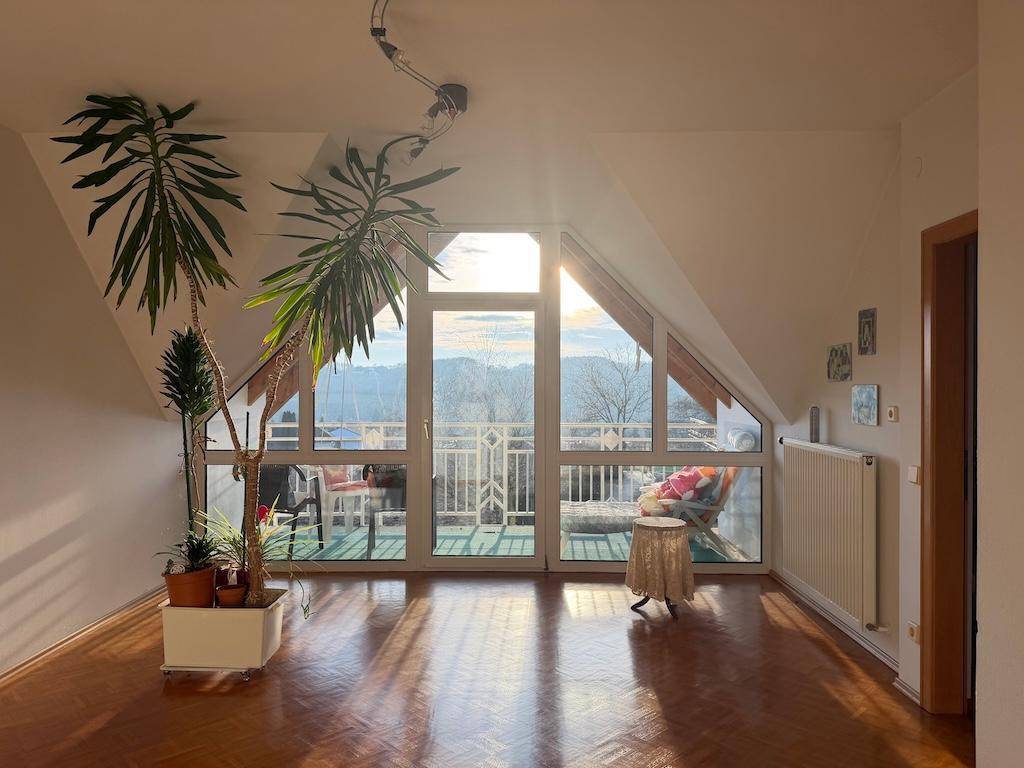 Helles Wohnzimmer im Dachgeschoss mit großen Fenstern und Panoramablick auf die Landschaft.