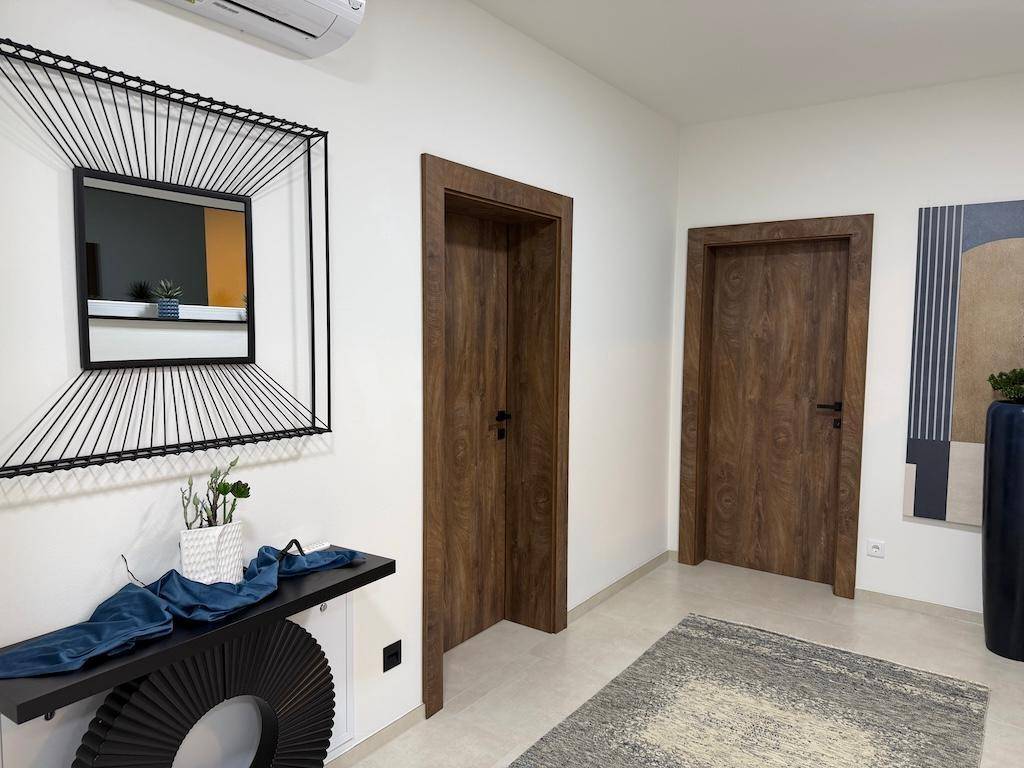 Heller Flur mit modernen Holztüren, einem dekorativen Spiegel und einer Konsole mit Pflanzen.