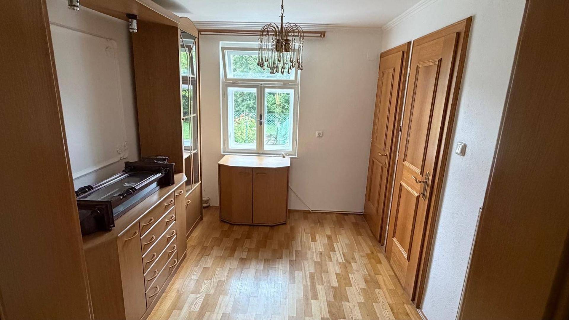 Heller Raum mit Holzparkett, großen Fenstern und traditionellen Holzschränken, ideal als Wohn- oder Esszimmer.