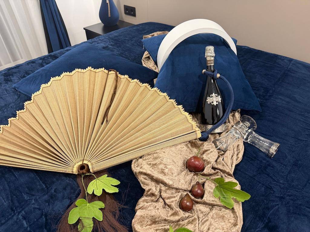 Dekorative Elemente auf einem Bett mit blauer Bettwäsche, inklusive Sektflasche und Fächer.