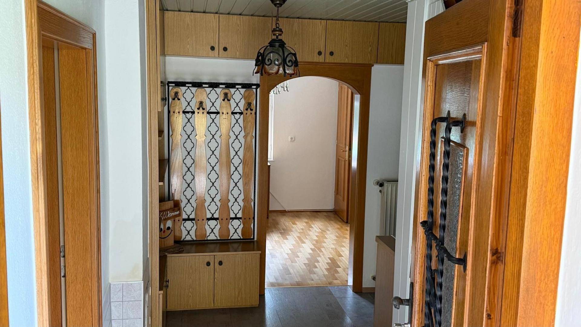 Eingangsbereich mit Garderobe, Holzböden und einem Bogen, der zu weiteren Räumen führt.