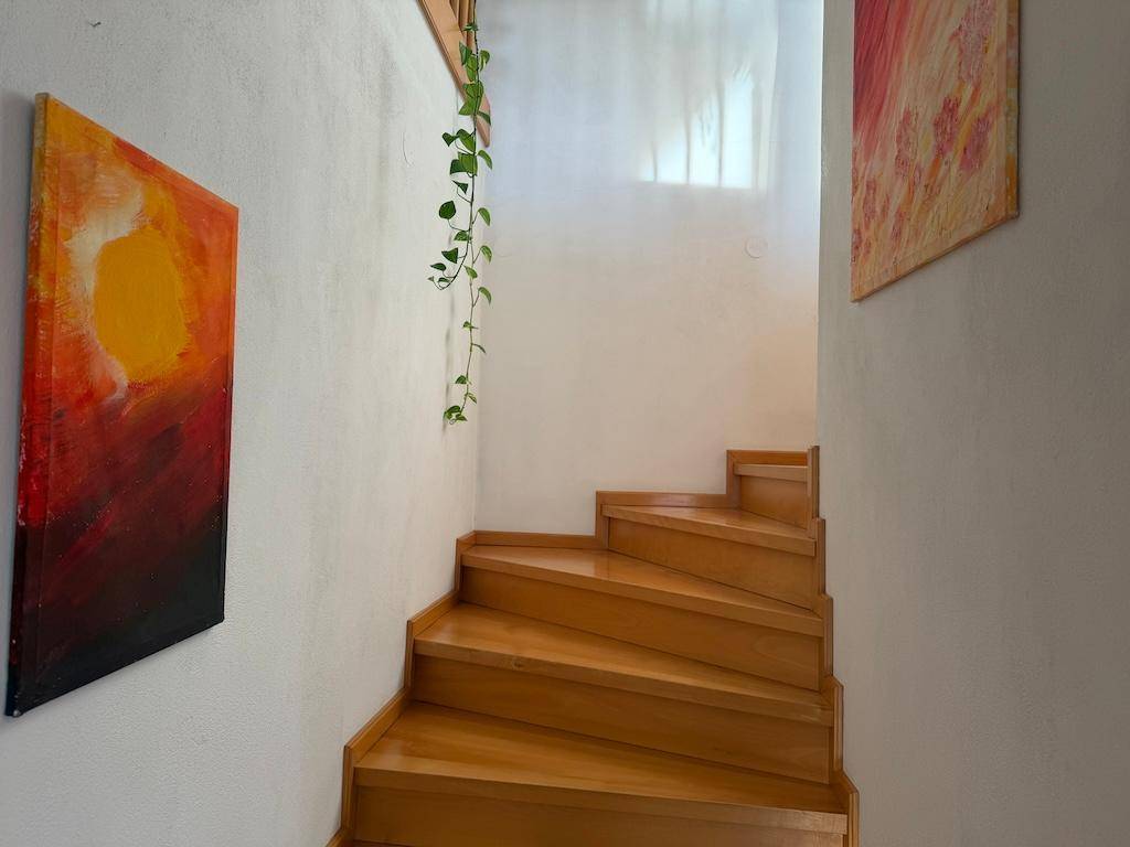 Helle Holztreppe führt nach oben, umgeben von weißen Wänden und moderner Kunst.
