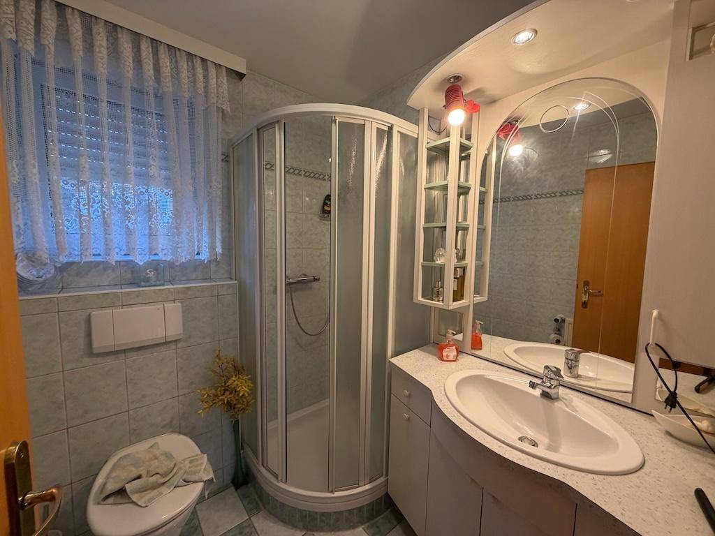 Badezimmer mit Eckdusche, Waschbecken und hellblauen Fliesen, funktional ausgestattet.