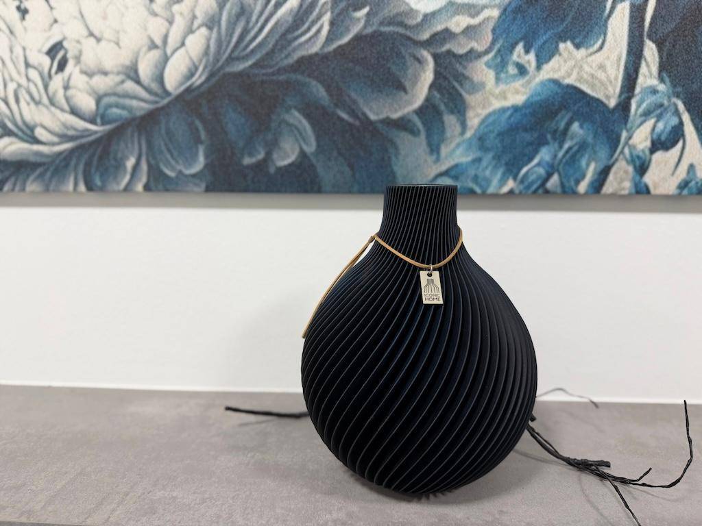 Detailaufnahme einer modernen schwarzen Vase mit zartem Anhänger auf einer Ablagefläche.
