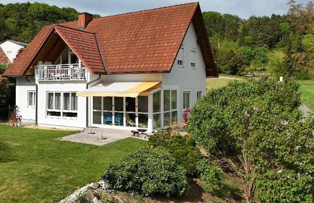 Attraktives Haus mit Balkon, Wintergarten und weitläufigem Rasen in grüner Umgebung.
