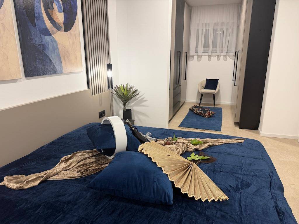 Schlafzimmer mit großem Bett, blauer Bettwäsche und Blick auf den Ankleidebereich.