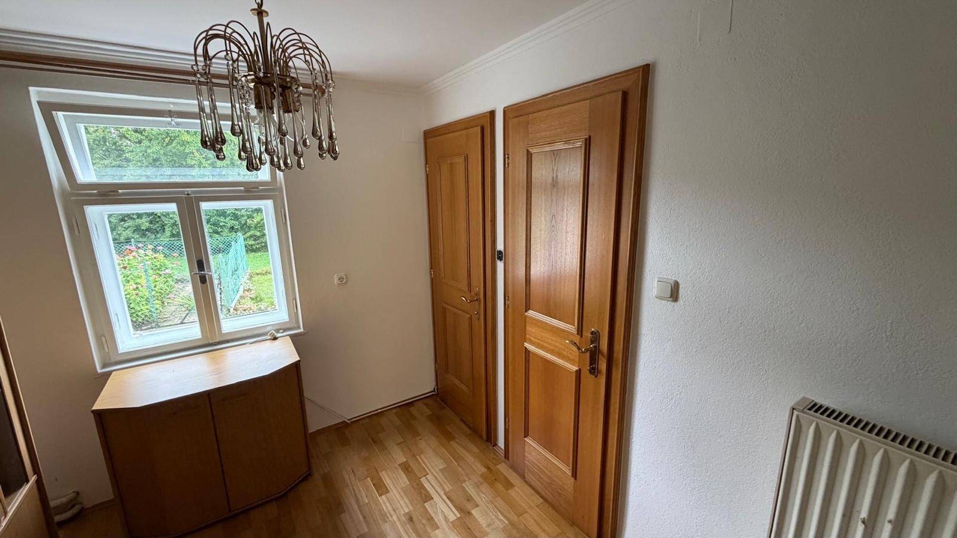 Helles Zimmer mit Parkettboden, Fenster und Holztüren, möglicherweise ein Schlafzimmer oder Büro.