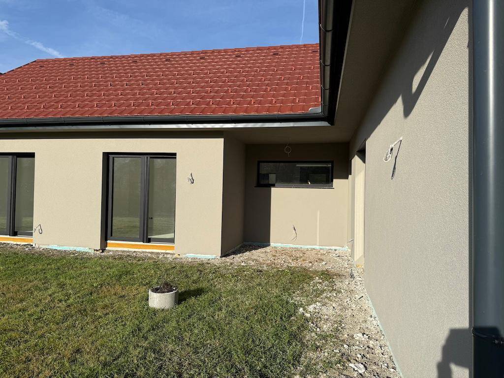 Detailansicht der Gebäudeecke mit Fenster und Regenrinne, umgeben von Rasen und Erde.