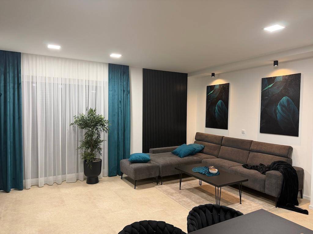 Helles Wohnzimmer mit einem bequemen Sofa, Wandkunst und großen Fenstern mit Vorhängen.