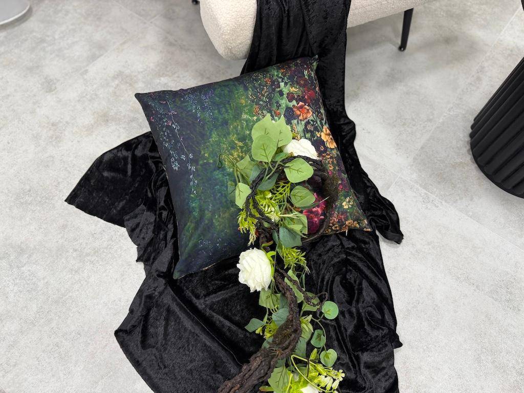 Detailaufnahme eines dekorativen Kissens mit floralem Muster und künstlichen Blumen auf schwarzem Stoff.