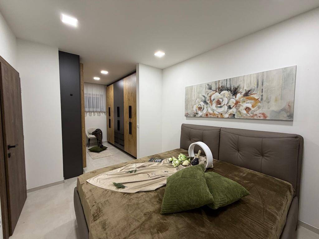 Modernes Schlafzimmer mit großem Bett, Kunstwerk und begehbarem Kleiderschrank im Hintergrund.
