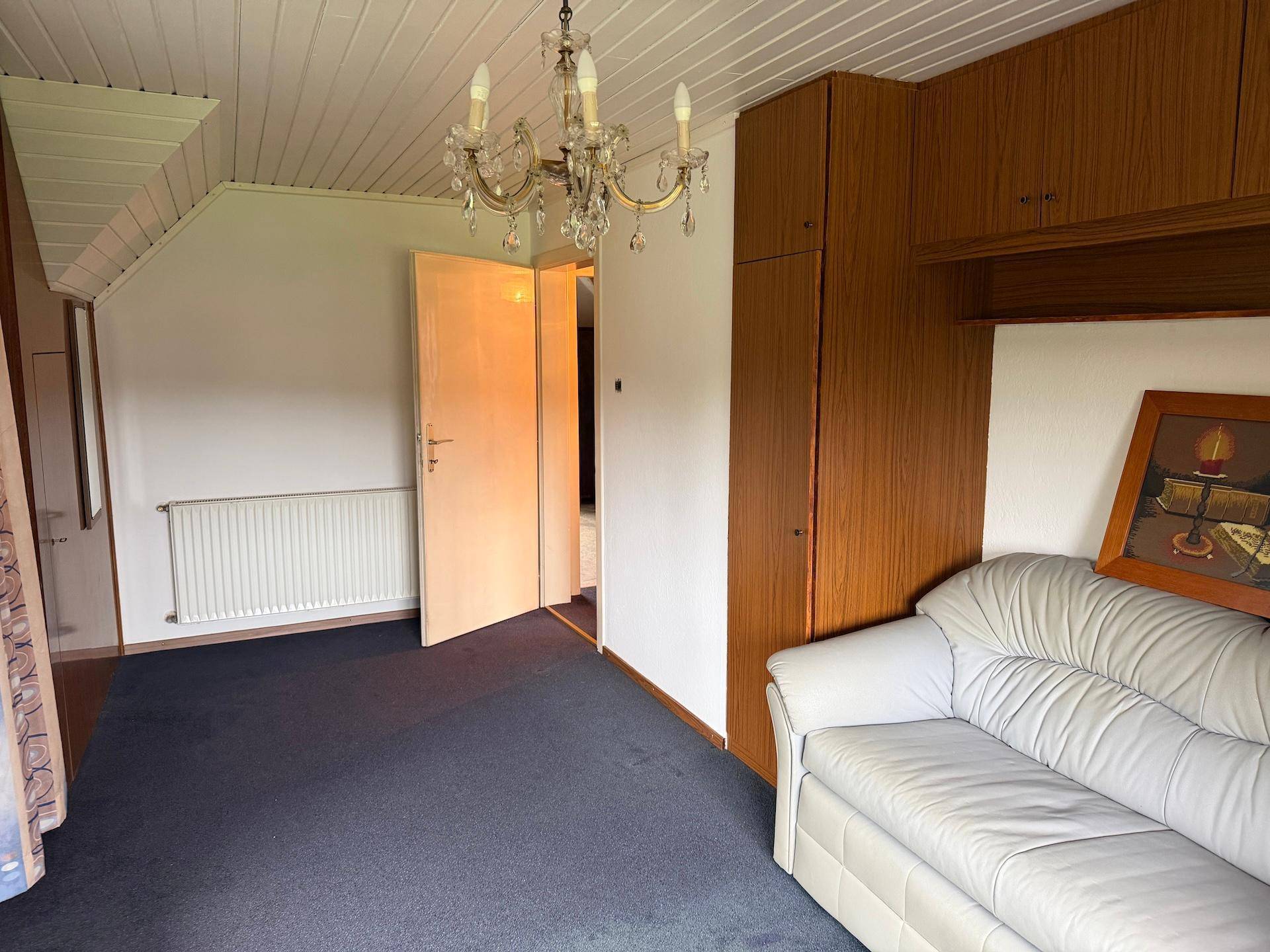 Helles Zimmer mit Teppichboden, Holzschränken und einem Fenster, das viel Tageslicht hereinlässt.