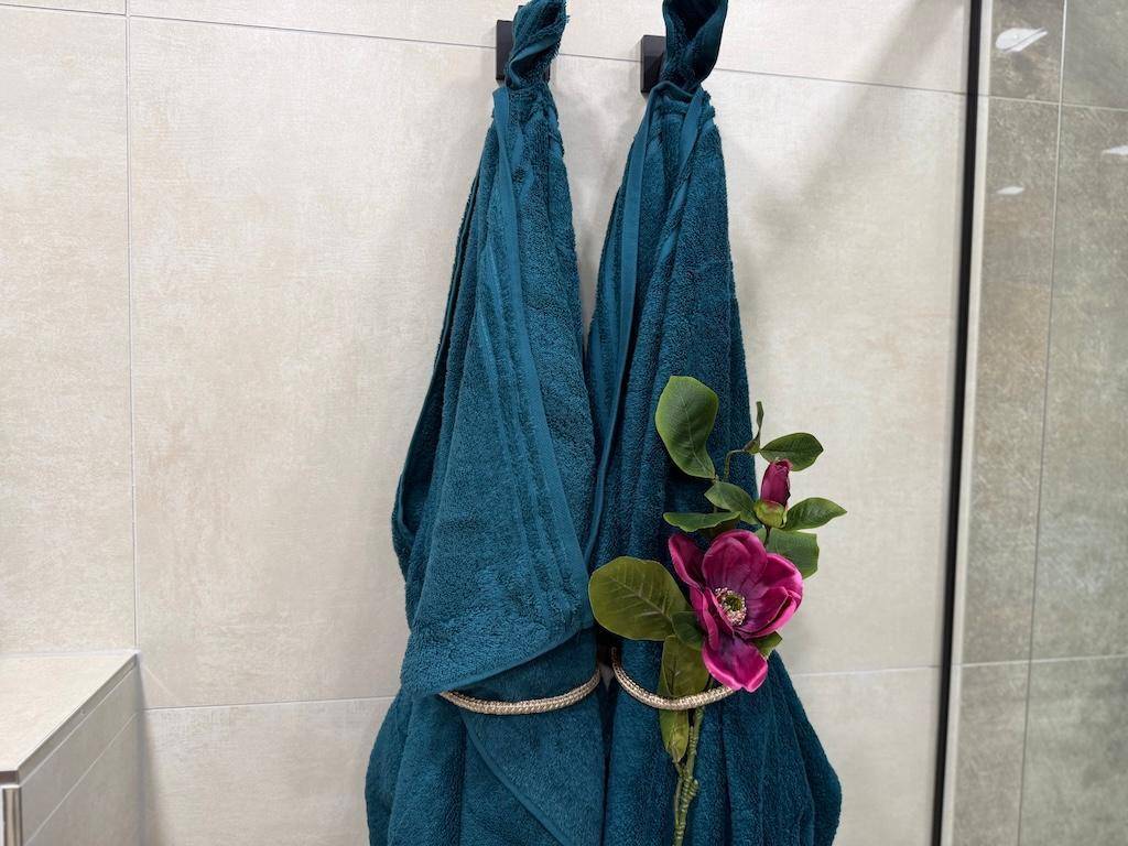 Detailansicht von zwei türkisfarbenen Handtüchern mit dekorativer Blume im modernen Badezimmer.