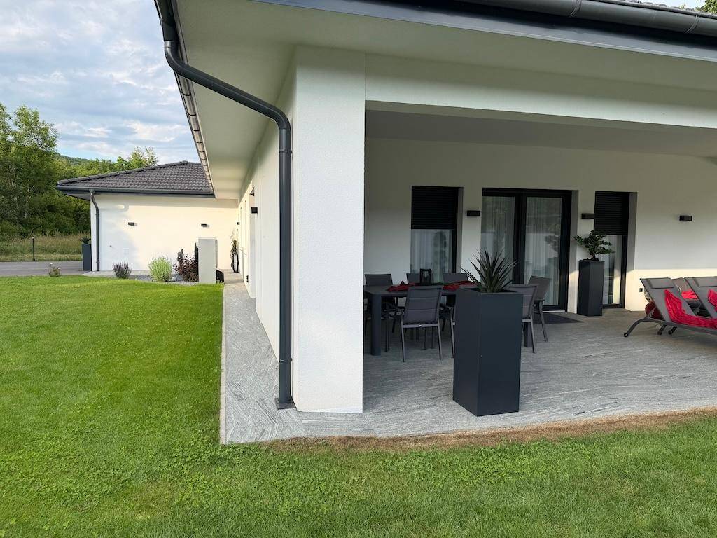 Modernes Einfamilienhaus mit weitläufigem Rasen und großer überdachter Terrasse, umgeben von viel Grün.