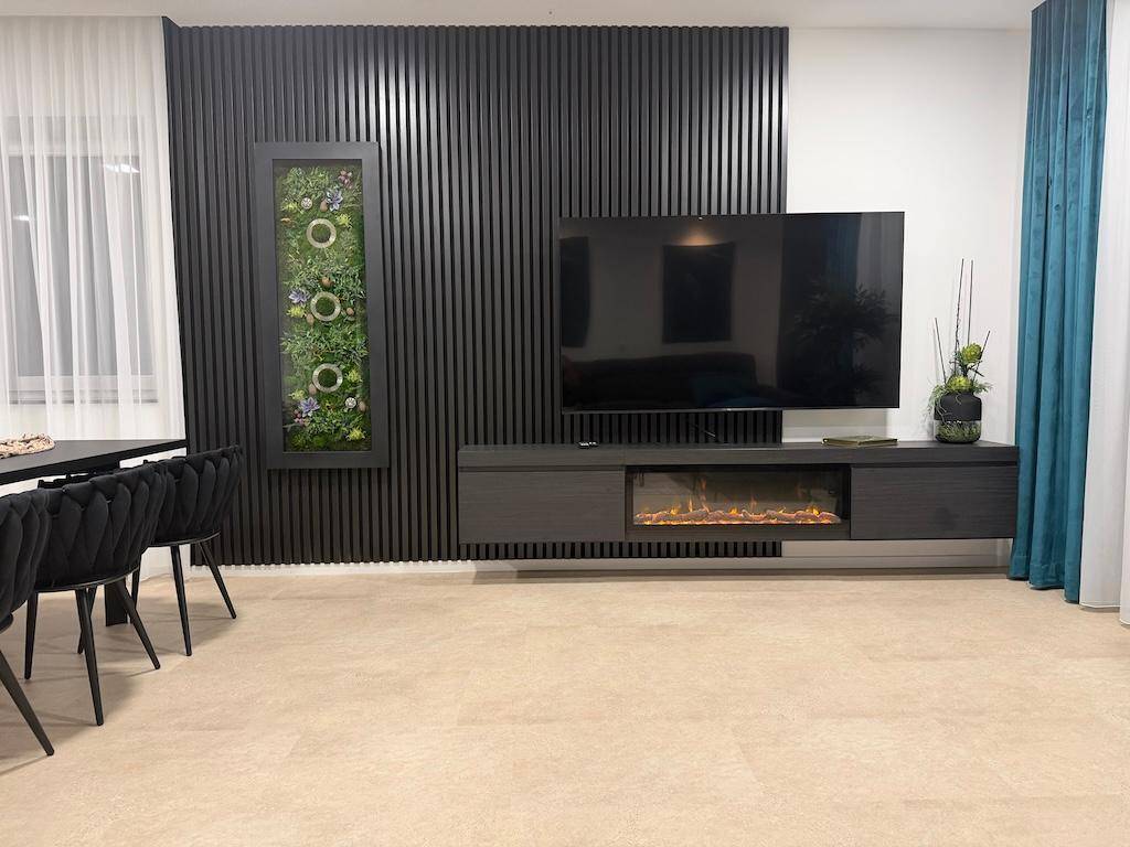 Moderner offener Wohn- und Essbereich mit dunklen Holzlamellen, großem Fernseher und elektrischem Kamin.