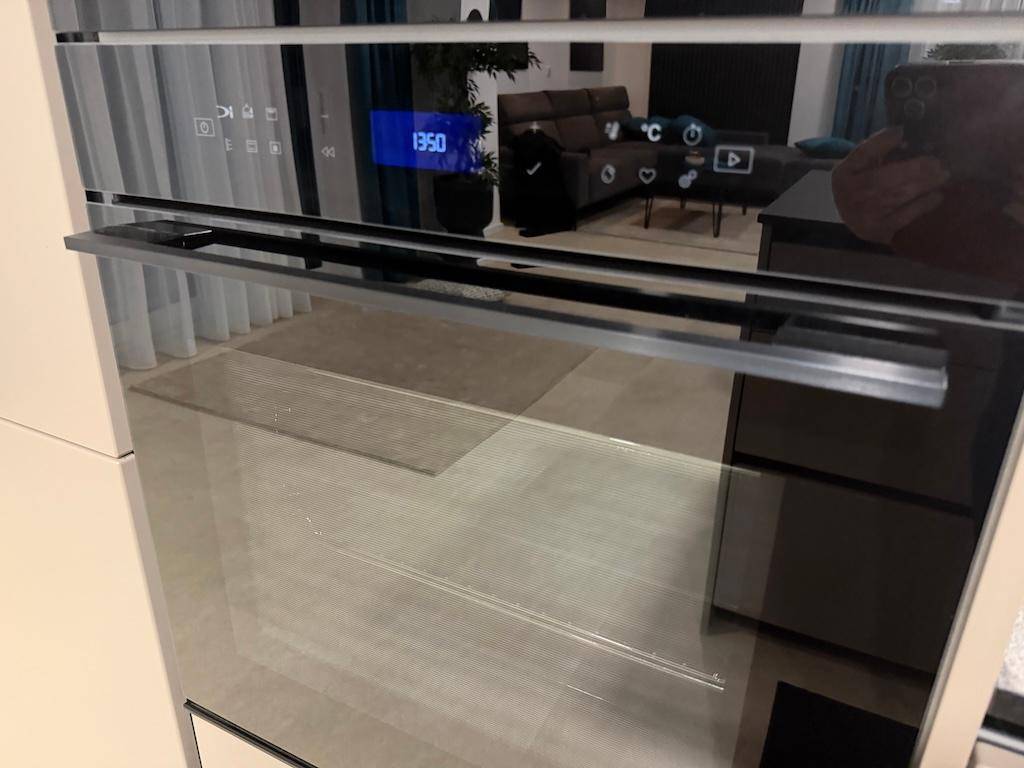 Geschlossener Backofen mit spiegelnder Oberfläche, die einen Teil des Wohnbereichs reflektiert.