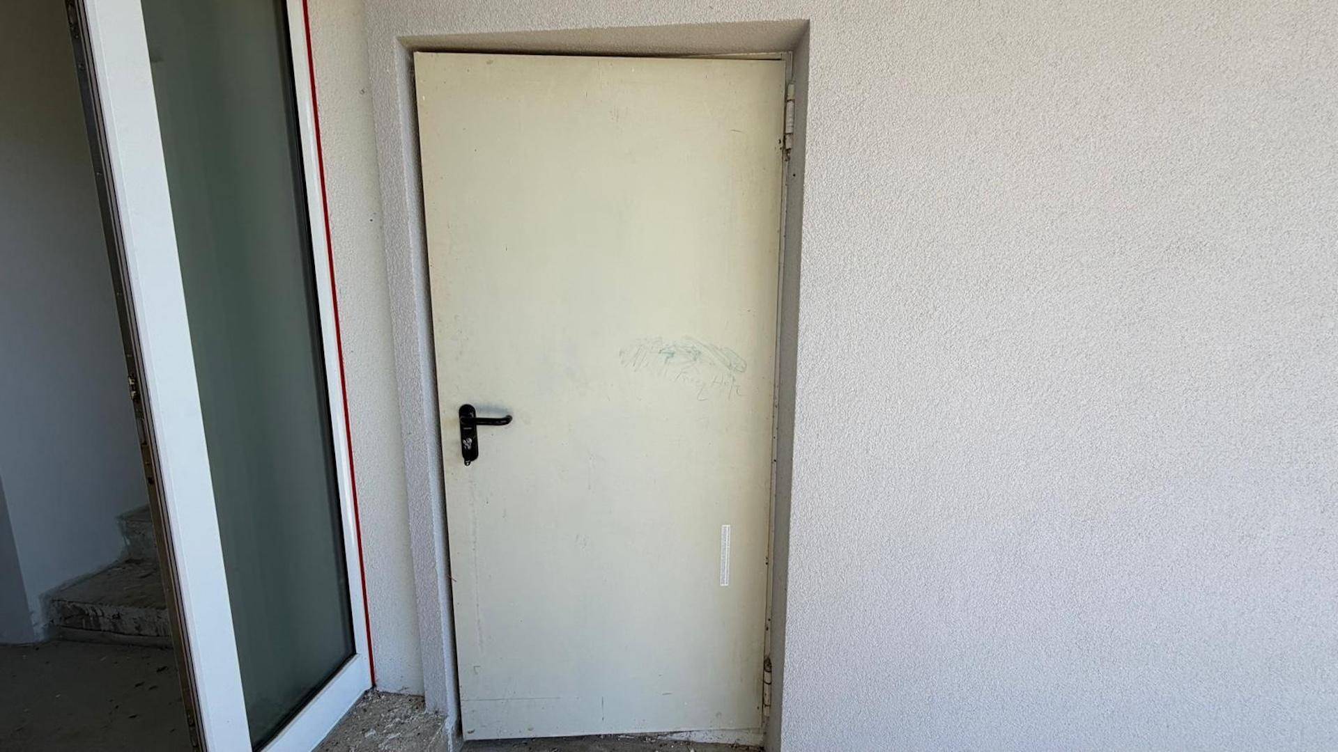 Einfache weiße Tür in einem noch unfertigen Innenbereich mit rauer Wandstruktur.