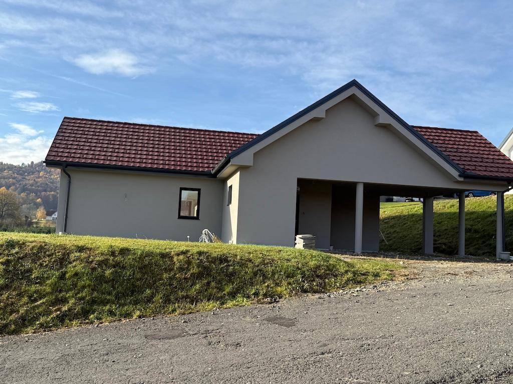 Ansicht des neuen Einfamilienhauses mit integriertem Carport und rotem Ziegeldach in ländlicher Umgebung.