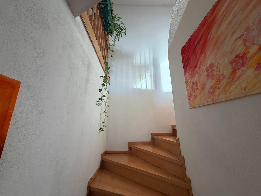 Helle Holztreppe führt nach oben, umgeben von weißen Wänden und farbenfroher Kunst.