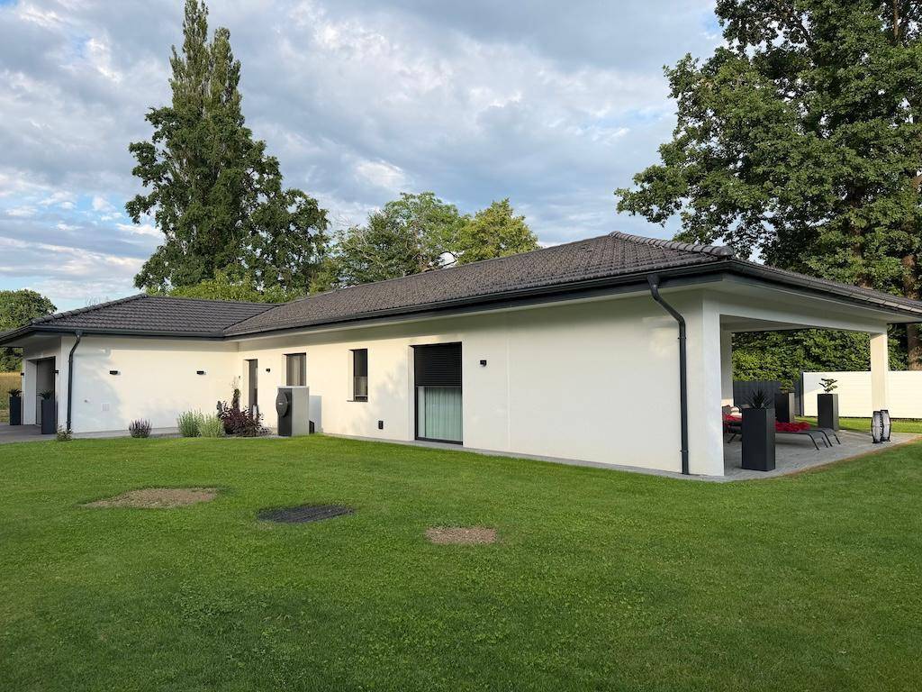 Modernes Einfamilienhaus mit weitläufigem Rasen und großer überdachter Terrasse, umgeben von viel Grün.