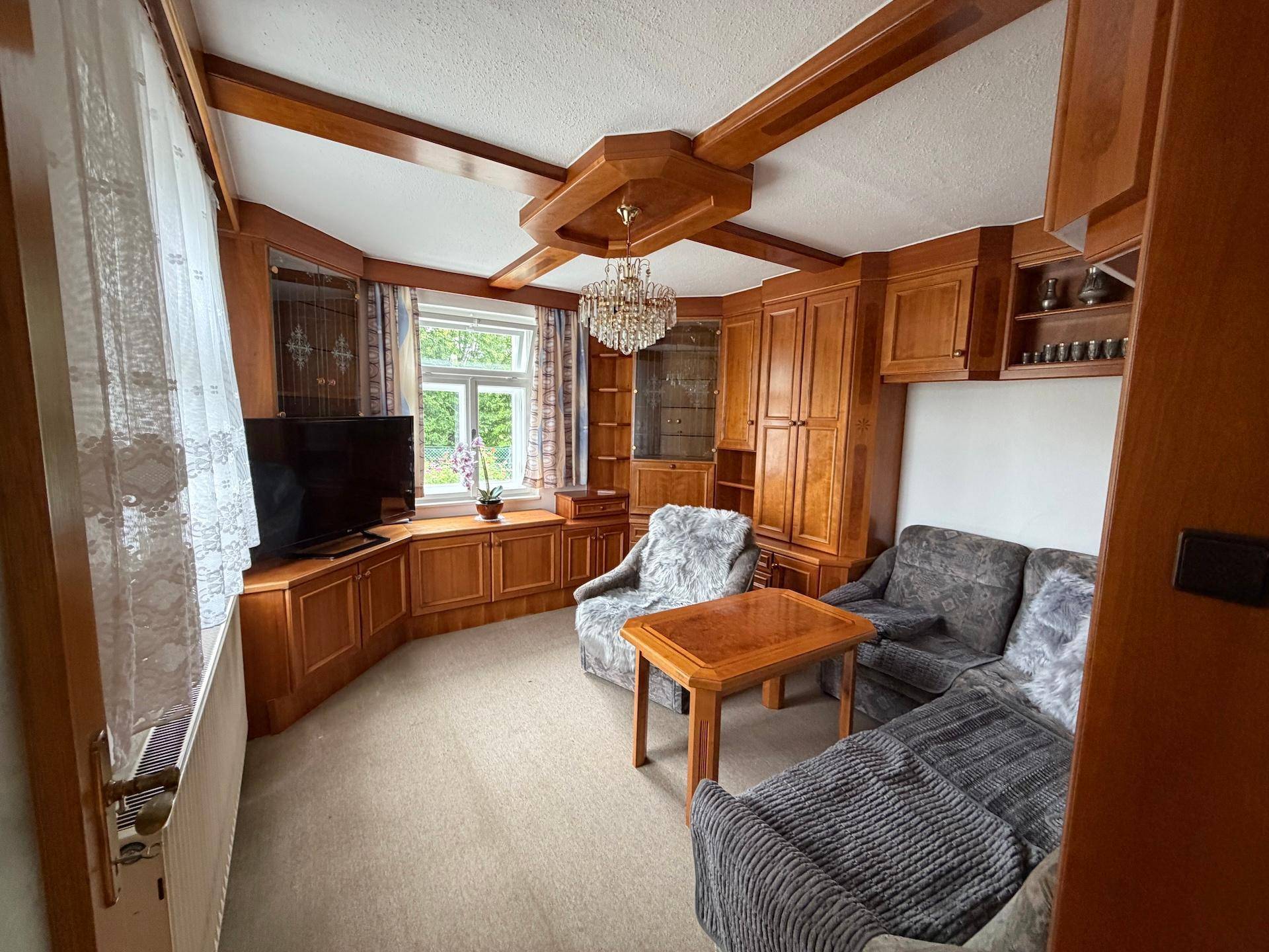 Gemütliches Wohnzimmer mit Holzvertäfelung, bequemen Sofas und einem Fenster mit Blick ins Grüne.