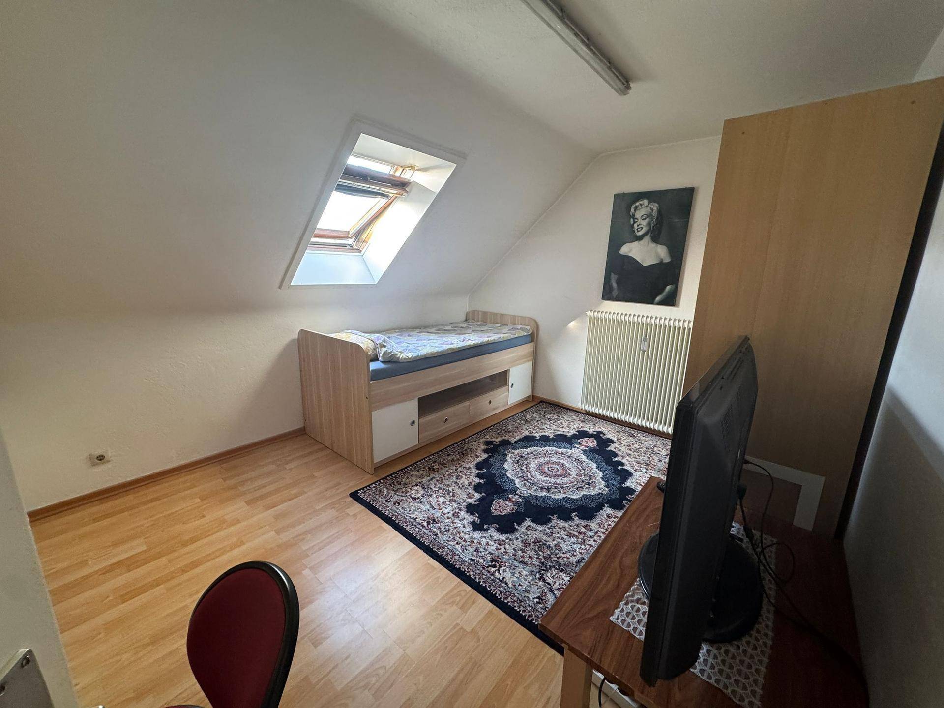 Schlafzimmer im Dachgeschoss mit Einzelbett, Teppich und einem Dachfenster.