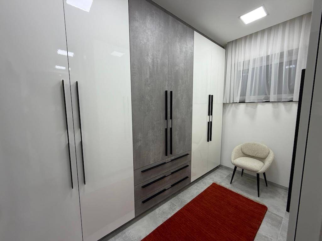 Moderner begehbarer Kleiderschrank mit glänzenden Schränken, einem Stuhl und einem roten Teppich.