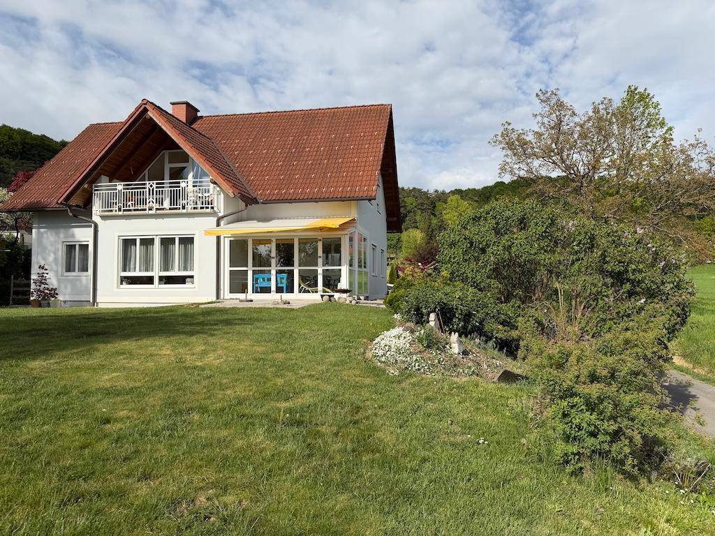 Wohnhaus mit weitläufigem Rasen, Balkon und Wintergarten in einer grünen Umgebung.