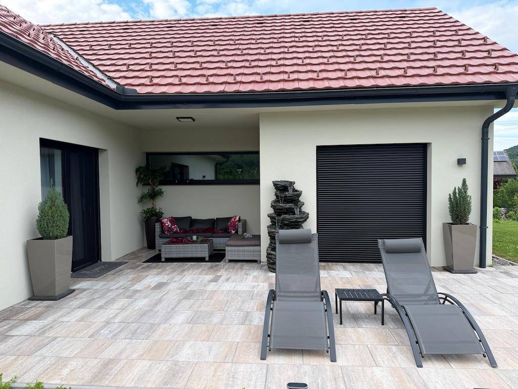 Attraktive Terrasse mit Sonnenliegen und einem dekorativen Wasserfall, angrenzend an eine überdachte Lounge.