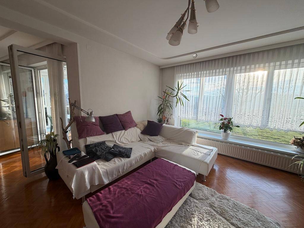 Gemütliches Wohnzimmer mit großem Sofa, Parkettboden und viel Tageslicht durch breite Fenster.