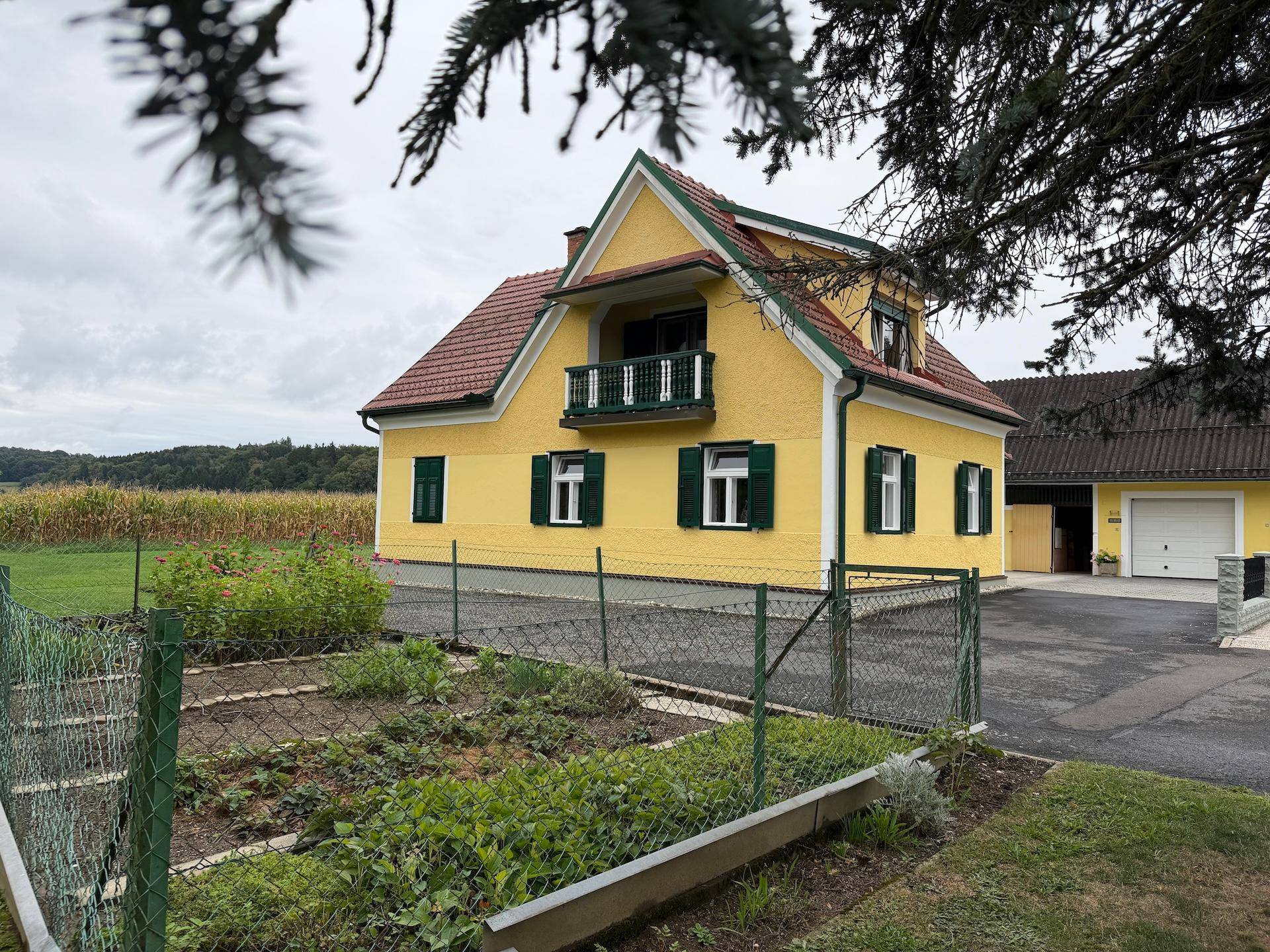 Ansicht des Hauses mit gelber Fassade und einem eingezäunten Gemüsegarten im Vordergrund.