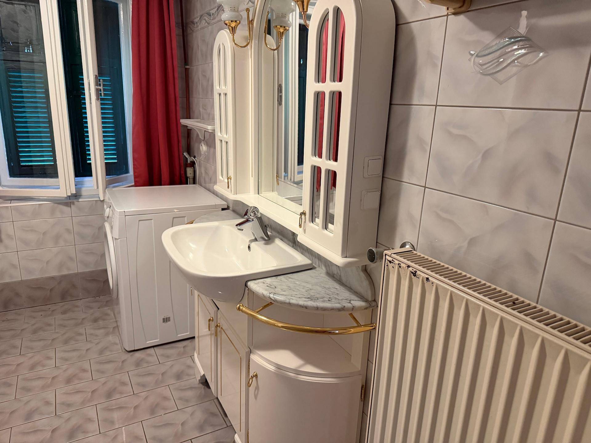 Badezimmer mit Waschbecken, Spiegel und Heizkörper, ausgestattet mit Fliesen und einem Fenster.