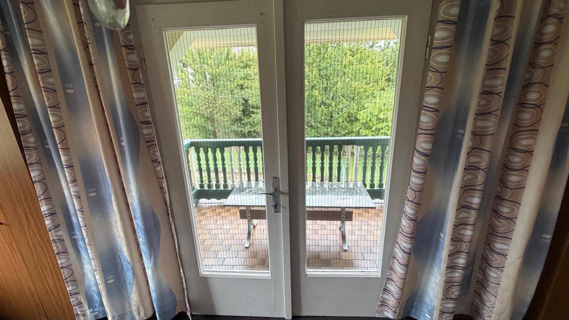 Blick aus einem Zimmer mit Vorhängen auf einen kleinen Balkon mit Tisch und Stühlen.