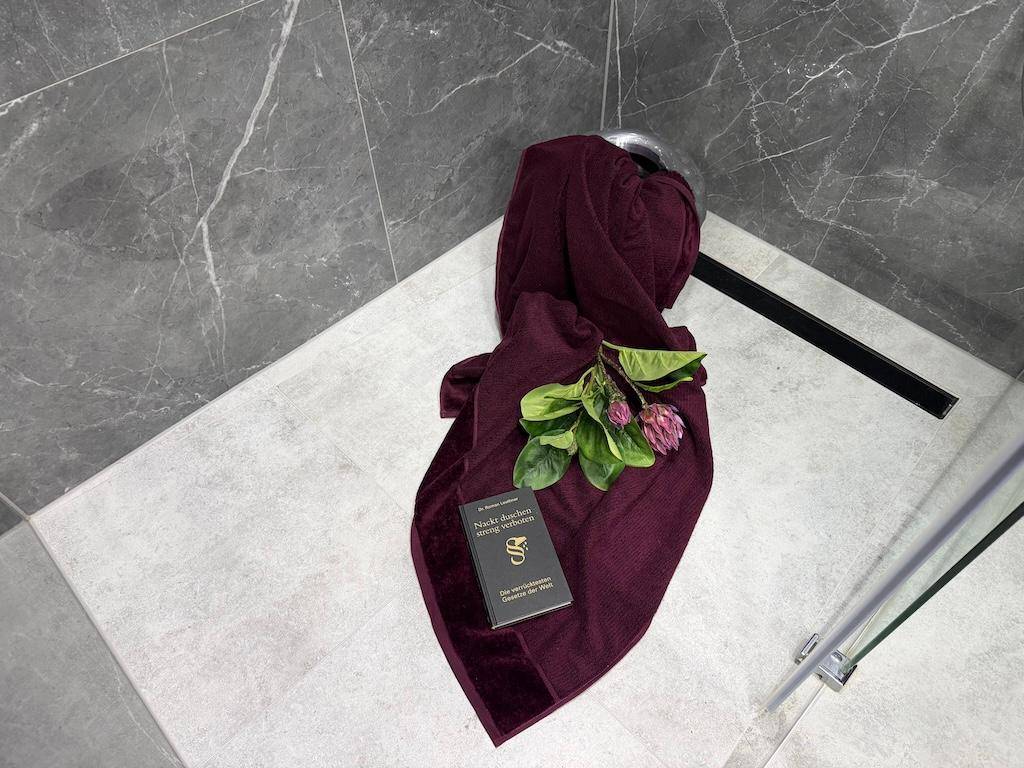Duschbereich mit eleganten Marmorfliesen am Boden und einem weichen lila Handtuch.
