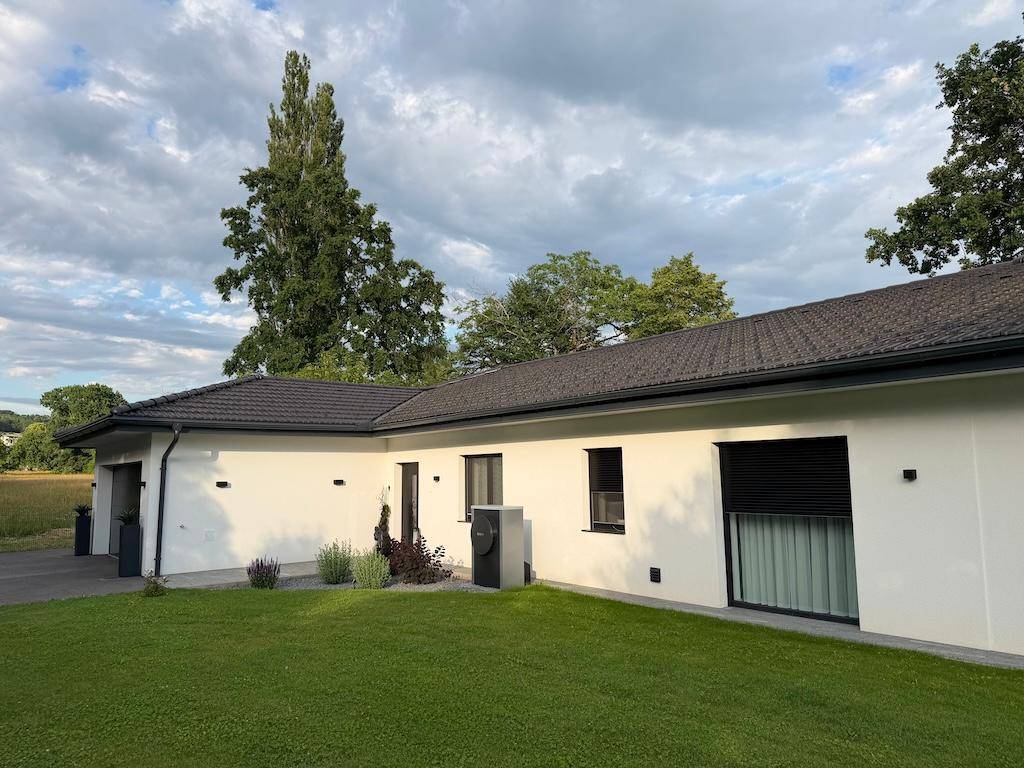 Seitenansicht des modernen Einfamilienhauses mit Wärmepumpe, gepflegtem Rasen und großen Fenstern.