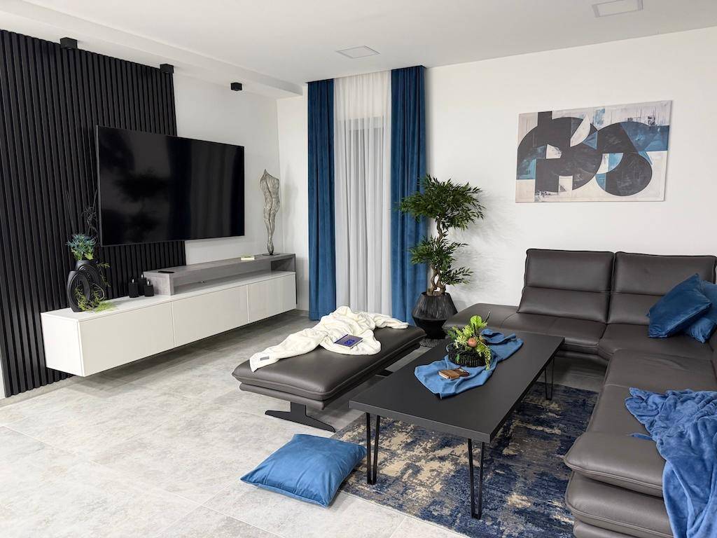 Modernes Wohnzimmer mit großem Fernseher, bequemer Eckcouch und stilvollen blauen Vorhängen.