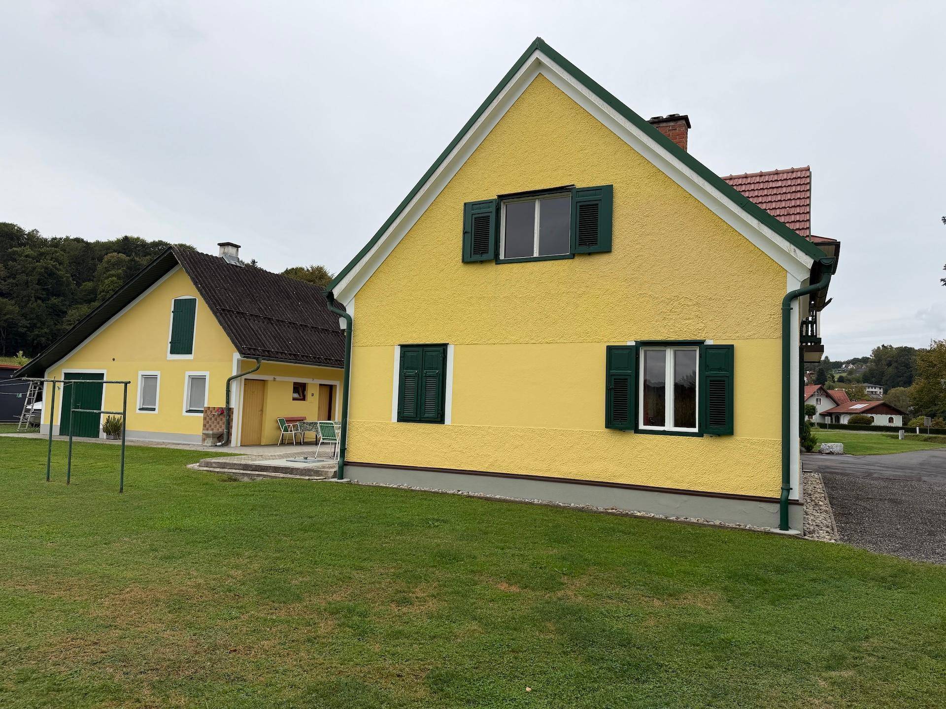 Seitenansicht des gelben Hauses mit grünen Fensterläden und einem weitläufigen Rasenbereich.