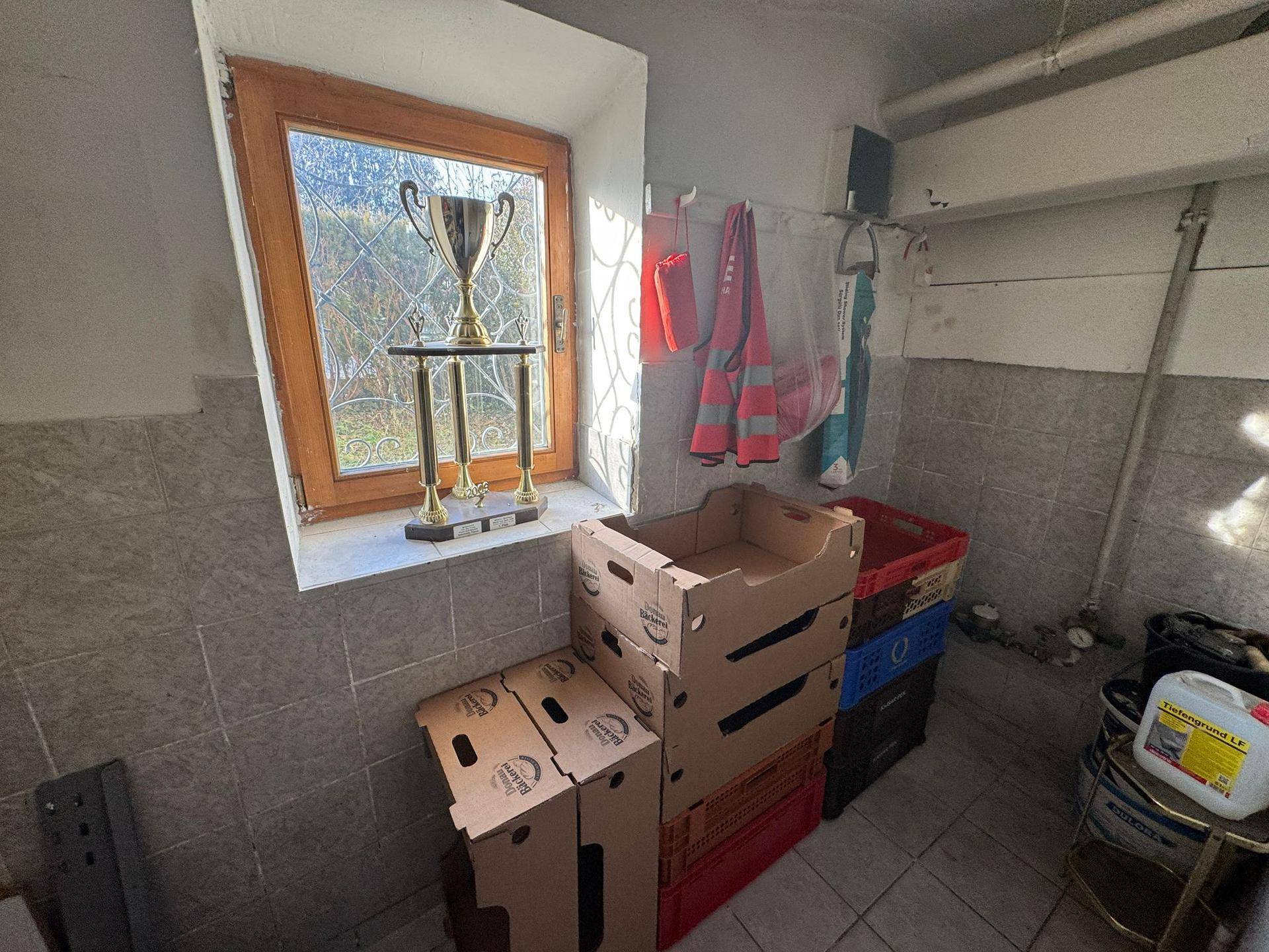 Kellerraum mit Fliesenboden, einem Fenster und verschiedenen Lagerkisten.