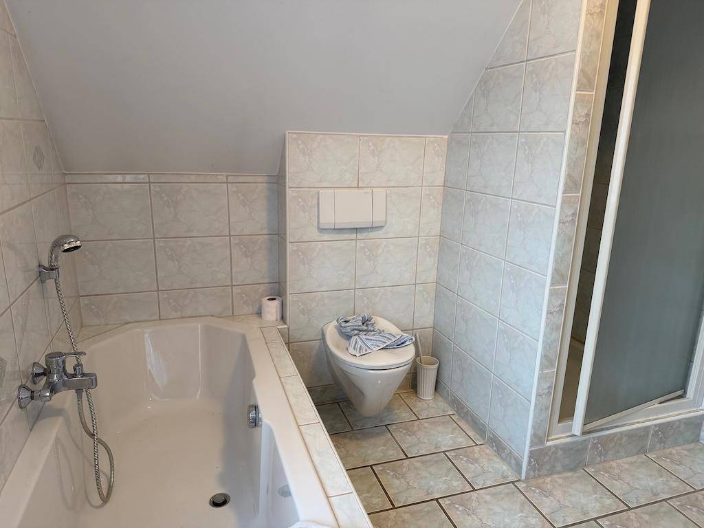 Nahaufnahme der Eckbadewanne und des wandhängenden WCs in einem gefliesten Badezimmer.