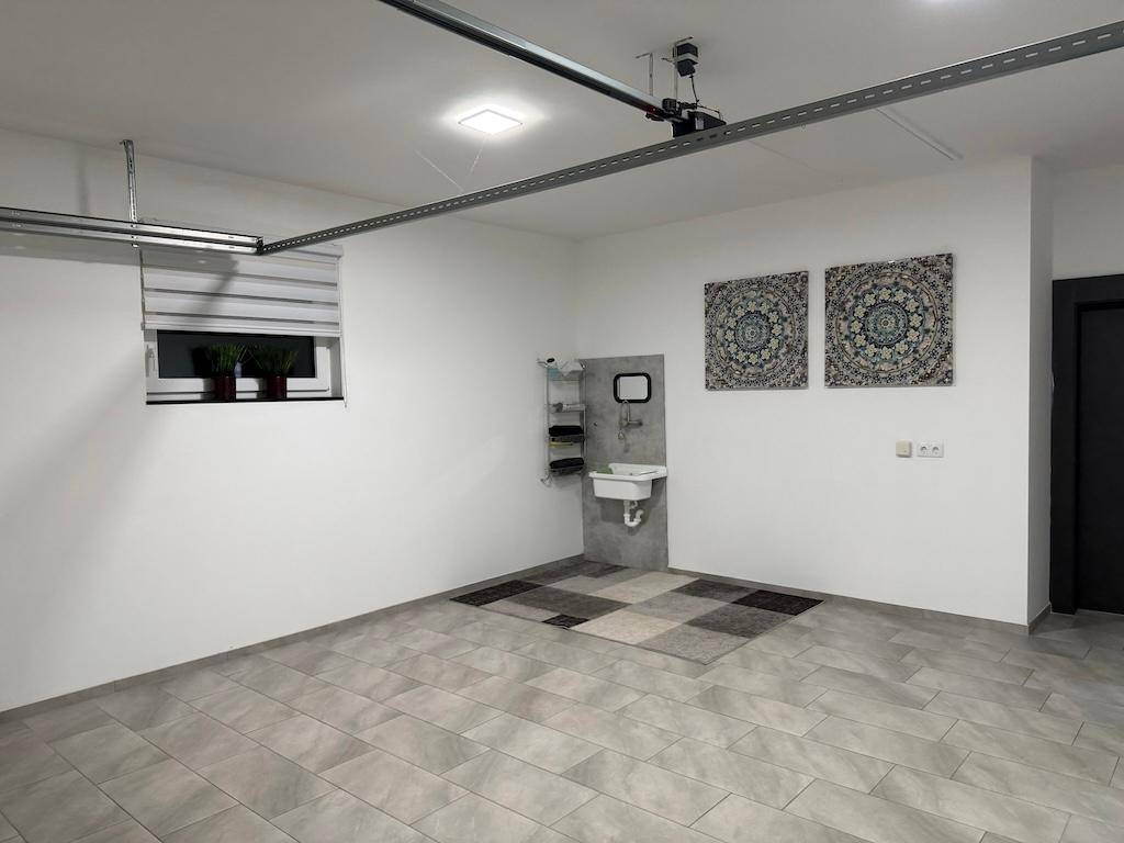 Geräumige Garage mit gefliestem Boden, einem Waschbecken und dekorativen Wandbildern.