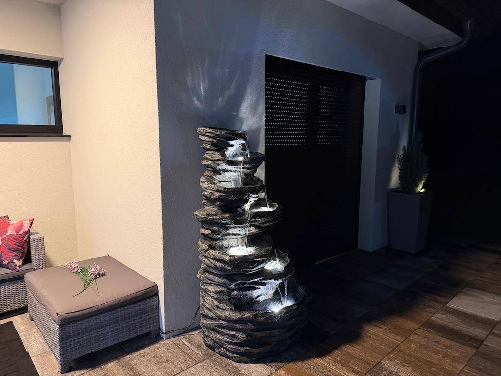 Gemütlicher Außenbereich bei Nacht mit beleuchtetem Felsenbrunnen und Sitzgelegenheiten.