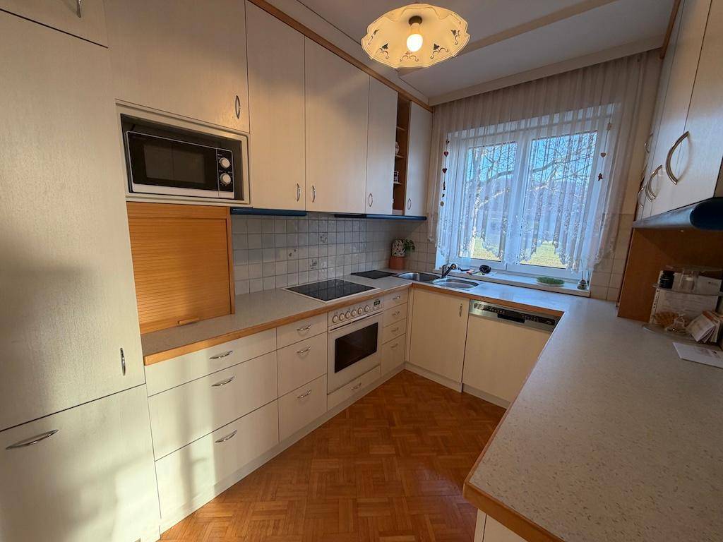 Gut ausgestattete Küche mit weißen Fronten, Kochfeld, Backofen und Spülmaschine.