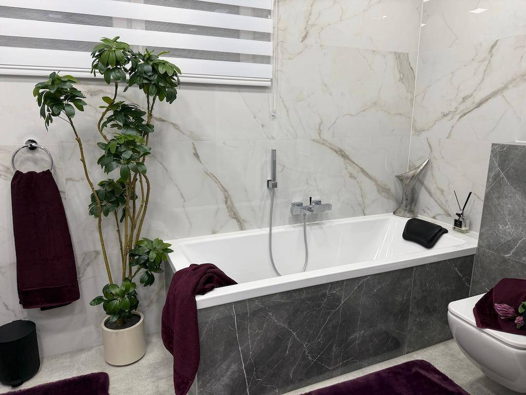 Elegantes Badezimmer mit Badewanne, Wand-WC und hochwertigen Marmorfliesen an Wänden und Boden.