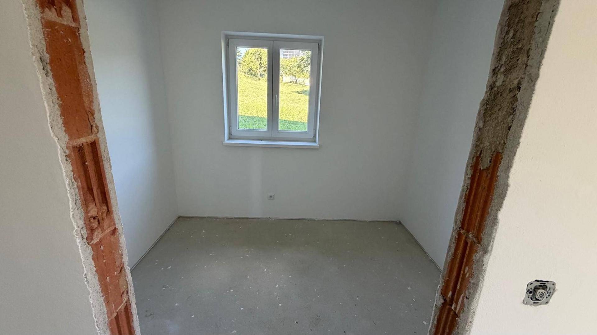 Leerer Raum im Rohbau mit einem Fenster, das einen schönen Blick ins Grüne bietet.