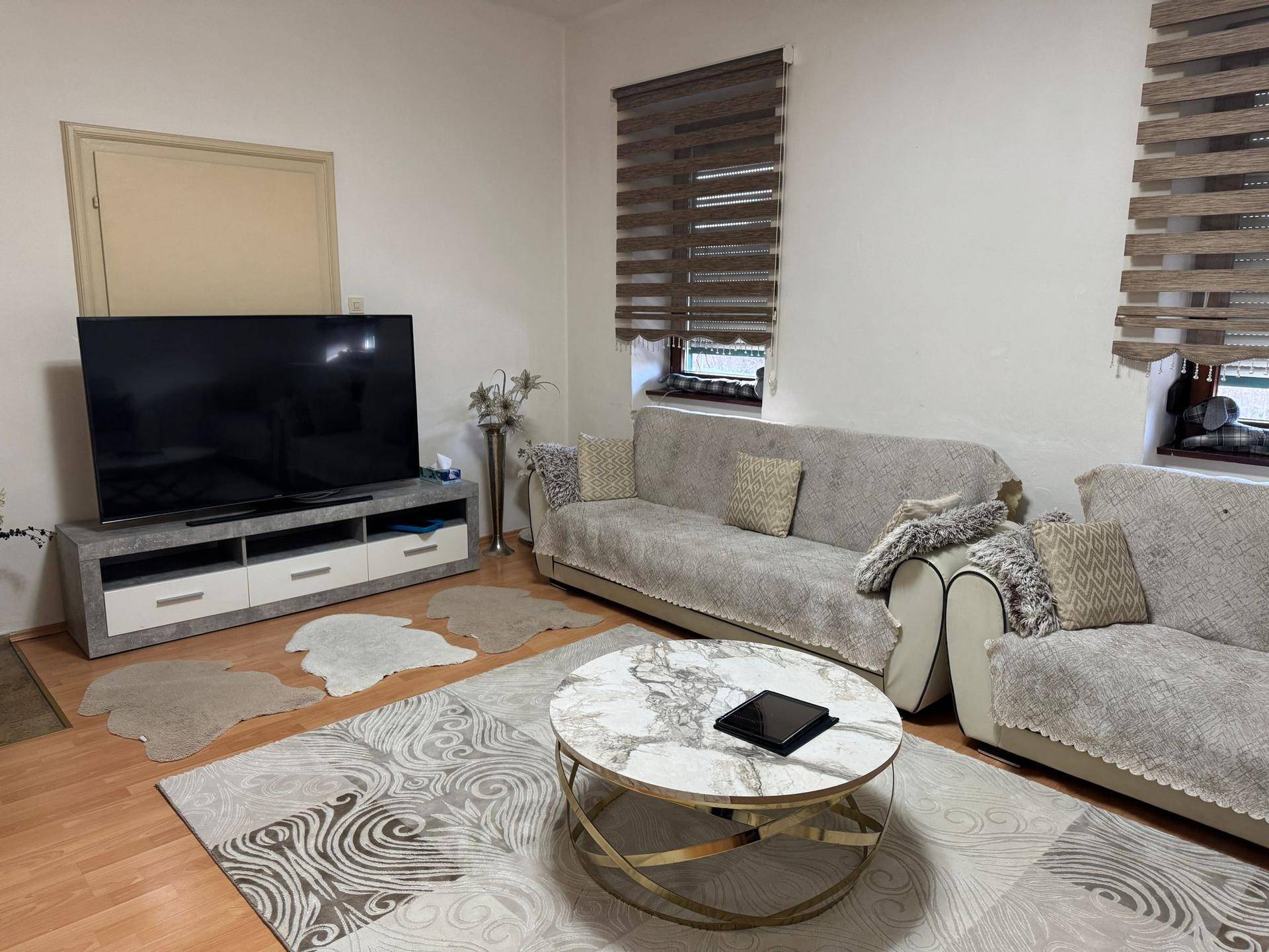 Gemütliches Wohnzimmer mit großem Fernseher, beigen Sofas und einem modernen Couchtisch.